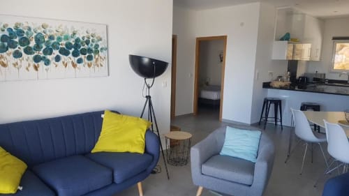 Séjour moderne à la Résidence Lésia à Corbara avec canapé bleu, fauteuil, œuvre d'art marine et cuisine ouverte.
