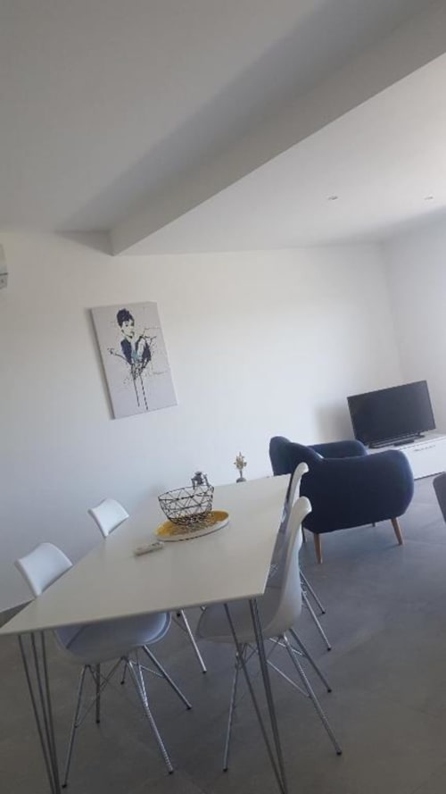 Espace repas contemporain de l'appartement Corbara avec table blanche, chaises noires, bureau avec télévision et œuvre d'art murale
