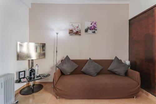 Modern sitting area in Suite T1 at Armação Beach Residences with brown sofa, gray pillows, wall art, and TV setup