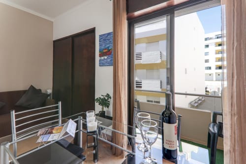 Modern apartment balcony at Armação Beach Residences with city view, wine bottle, glasses, and coastal building backdrop