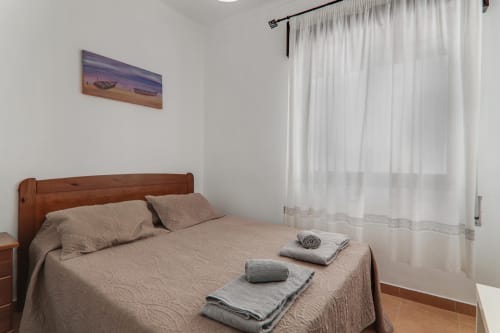 Bright bedroom in Armação de Pêra suite with wooden bed, beige linens, white curtains, and coastal artwork
