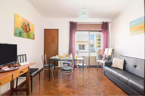 Cozy apartment living area at Armação Beach Residences with dining table, gray sofa, TV, and balcony overlooking city