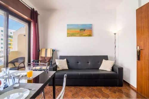 Modern apartment living room at Armação Beach Residences with black sofa, dining area, and city view balcony
