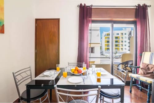 Dining area in Armação Beach Residences apartment with city views, set table, orange juice, and balcony overlooking resort