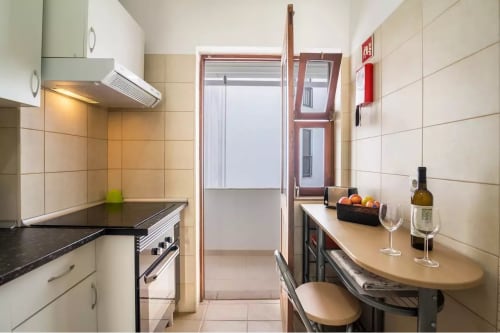 Modern kitchen and dining area in Armação Beach Residences apartment with black countertops, white cabinetry, and balcony