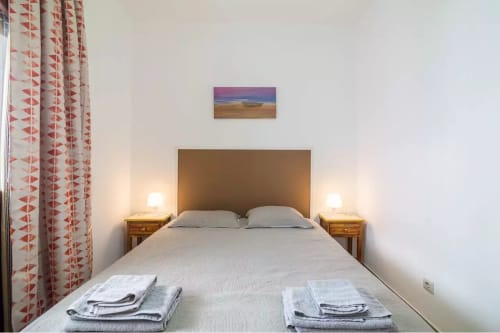 Bedroom at Armação Beach Residences with queen bed, bedside lamps, wooden nightstands, and red patterned curtains