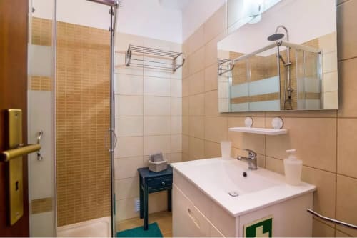 Modern bathroom in Armação Beach Residences apartment with beige tiled walls, glass shower enclosure, white sink vanity, and