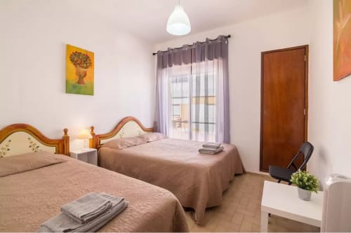 Bright twin bedroom at Armação Beach Residences with wooden beds, balcony doors, and city views in Armação de Pêra