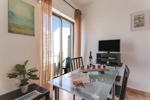 Modern apartment living area at Armação Beach Residences with glass dining table, TV, balcony access, and city views
