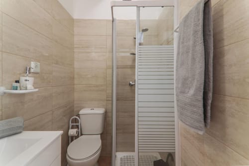 Modern bathroom with walk-in shower, white toilet, heated towel rack, and beige tile walls at Armação Beach Residences