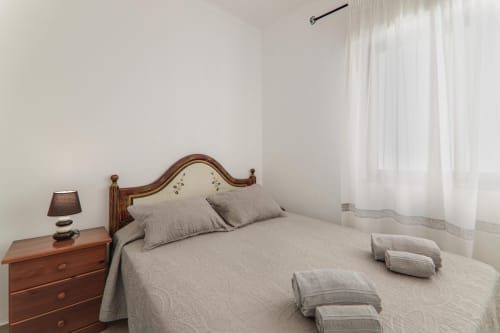 Bright bedroom at Armação Beach Residences with wooden headboard, gray bedding, nightstand lamp, and sheer curtains in