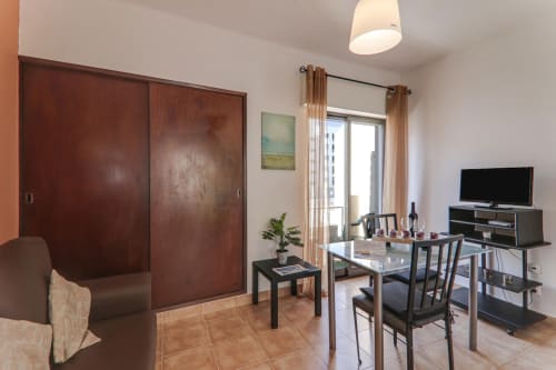 Modern apartment living area at Armação Beach Residences with dining table, TV, wooden wardrobe, and balcony access in