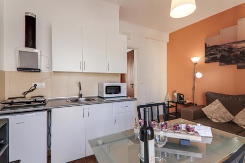 Modern kitchen and living area in Suite T1 at Armação Beach Residences, featuring white cabinets, dining table, and orange