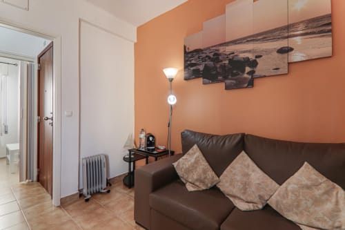 Modern apartment sitting area at Armação Beach Residences with brown leather sofa, orange accent wall, and coastal décor in