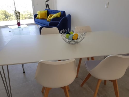 Espace repas moderne à la Résidence Lésia Corbara avec table blanche, chaises crème, coupe de fruits et canapé bleu en arrière-plan