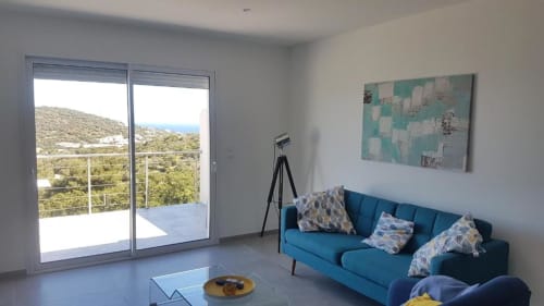 Séjour moderne à la Résidence Lésia à Corbara avec canapé bleu, vue sur mer et balcon surplombant le paysage méditerranéen