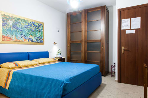 Camera da letto con letto matrimoniale blu presso l'Affittacamere Al Mare a Torre Grande, armadio in legno, cuscini gialli e opere d'arte