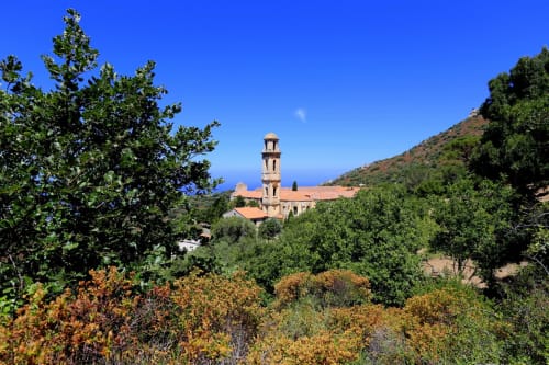Église en pierre traditionnelle avec clocher entourée de végétation méditerranéenne surplombant la côte près de Corbara, Corse