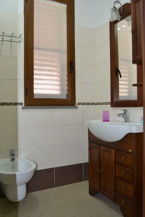 Bagno moderno con piastrelle bianche, mobile lavabo in legno, lavandino bianco, toilette e due armadietti specchio presso Affittacamere Al