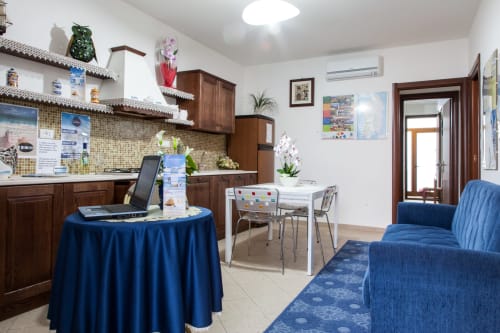 Zona comune moderna dell'hotel Al Mare a Torre Grande con sedute blu, angolo cottura, tavolo da pranzo e area di lavoro