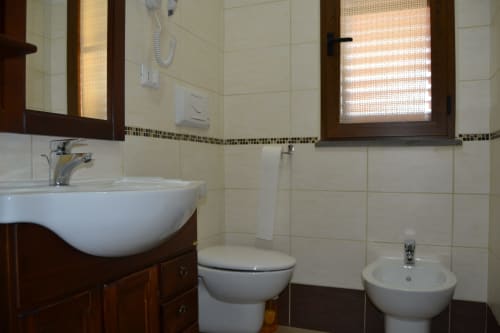Salle de bain moderne avec carrelage blanc, meuble vasque en bois foncé, toilettes et bidet à Affittacamere Al Mare, Torre Grande Oristano
