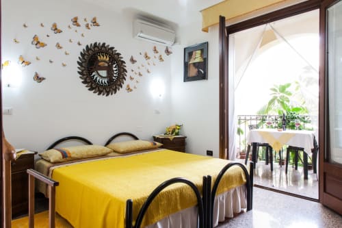 Camera da letto luminosa con biancheria gialla, decorazione murale farfalle, specchio ornato e balcone con vista giardino presso Affittacamere Al