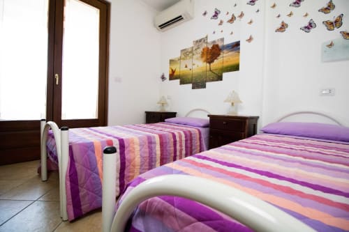 Chambre familiale lumineuse avec deux lits à rayures violettes, meubles en bois foncé, décalcomanies papillons et vue sur le jardin à Al Mare