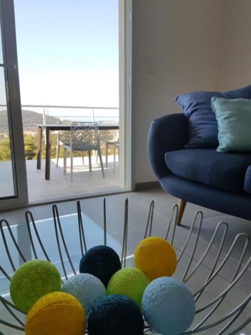Appartement moderne à Corbara avec vue mer, fauteuil bleu, pelotes de laine colorées dans un panier métallique, coin repas sur balcon