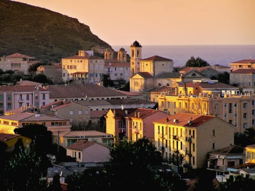 Coucher de soleil doré sur le village de Corbara avec ses bâtiments colorés et clocher d'église dominant la Méditerranée