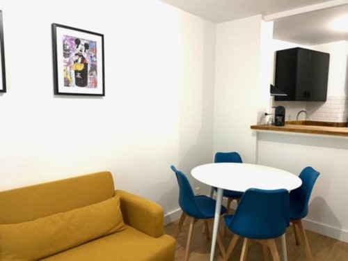 Espace de vie moderne à la Résidence Disneyland Place Toscane avec canapé jaune, table ronde blanche et chaises bleues
