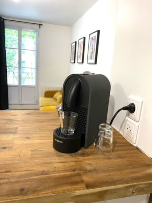 Machine à café noire sur table en bois dans un appartement de Disneyland Paris avec chaise jaune et tasses en verre à proximité