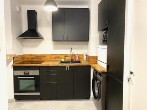Cuisine moderne entièrement équipée avec armoires noires, plan de travail en bois, cuisinière à gaz et lave-linge à la Résidence Disneyland