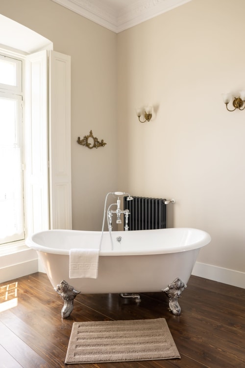 Elegante bañera con patas de garra en la Habitación Miyares de La Venta de Miyares, con accesorios cromados y apliques de pared ornamentados