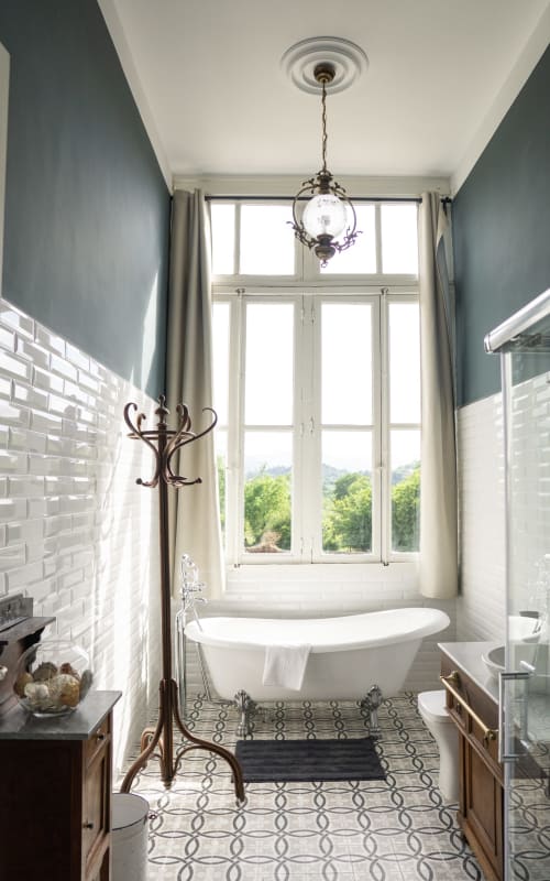 Elegant bathroom at La Venta de Miyares with freestanding bathtub, white tile, blue accent walls, and large window
