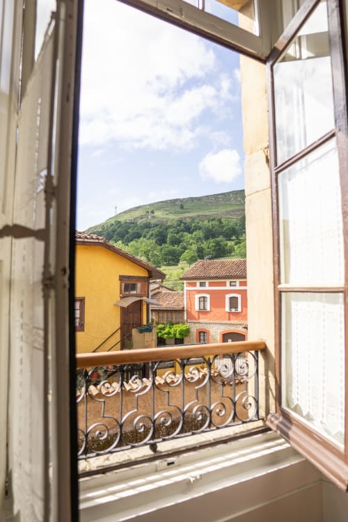 Open window view from El Palacio room at La Venta de Miyares showing colorful colonial buildings and green Asturian hillside