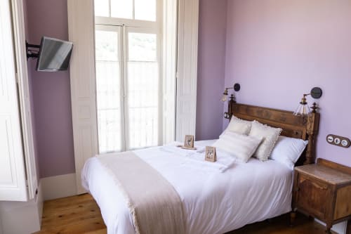 Dormitorio de la Suite Pintueles en La Venta de Miyares con paredes púrpura, cama de madera, ropa blanca y puertas hacia balcón con vistas