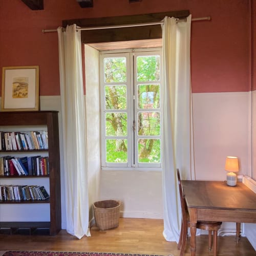 Chambre élégante aux murs en terre cuite, bibliothèque, bureau en bois et portes-fenêtres donnant sur les jardins