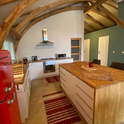 Cuisine de ferme moderne aux Lumieres Du Causse avec électroménagers rouges, poutres en bois, ilot central et murs d'accent verts