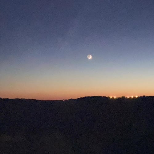 La lune se lève sur les champs obscurs au crépuscule, des lumières lointaines visibles à l'horizon près des Lumières du Causse