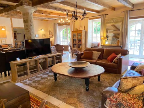 Spacieux séjour aux Lumieres Du Causse avec poutres en bois, canapé en cuir marron, table basse ronde et portes-fenêtres