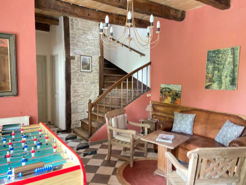 Salon rustique aux Lumières du Causse avec baby-foot, canapé en cuir, poutres apparentes et murs corail à Bellefont-la-Rauze