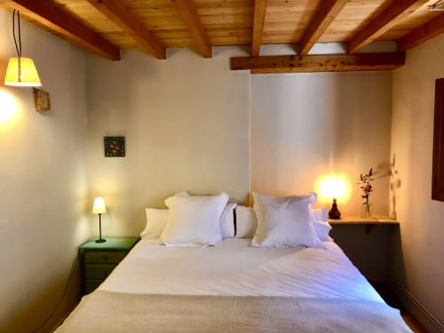 Dormitorio acogedor en Casa Tapiolas de Molló con vigas de madera, ropa de cama blanca, iluminación cálida y vistas a las montañas