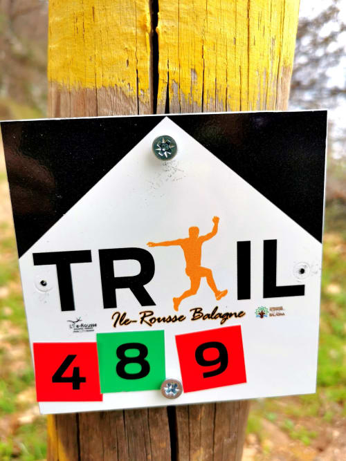 Marqueur de sentier de la route de randonnée Île-Rousse Balagne près de Corbara indiquant la distance 489km sur poteau en bois jaune