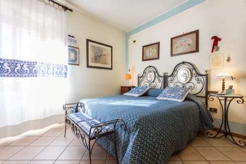 Affascinante camera da letto al Dormire Assisi B&B con arredamento blu e bianco, letto in ferro battuto ornato, vista sulla città e stile tradizionale assisiano