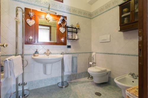 Bagno spazioso al Dormire Assisi B&B con lavabo su colonna, toilet, bidet e specchio decorativo a forma di cuore
