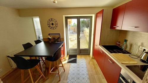 Cuisine-salle à manger moderne à La Maison De Fleurat : armoires rouges, table noire, portes sur jardin et horloge