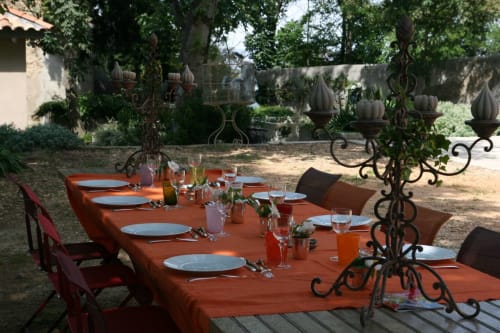 Espace repas extérieur au jardin de Campagne d'Albert avec nappe orange, couverts dressés et jardinières en fer forgé
