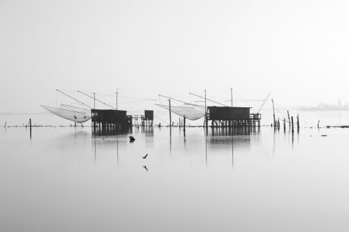 Traditional fishing stilt houses reflected in calm water near Bologna, Italy