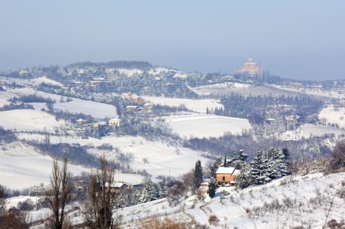 Snowy Tuscan hills with scattered buildings and cypress trees near Bologna, Italy