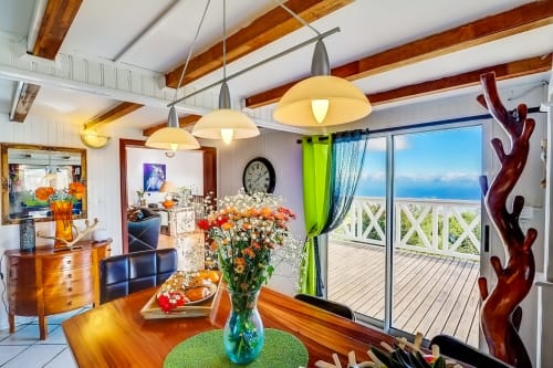 Salle à manger moderne avec vue sur mer aux Terrasses Du Volcan, Tampon. Poutres en bois, luminaires suspendus, fleurs fraîches et océan